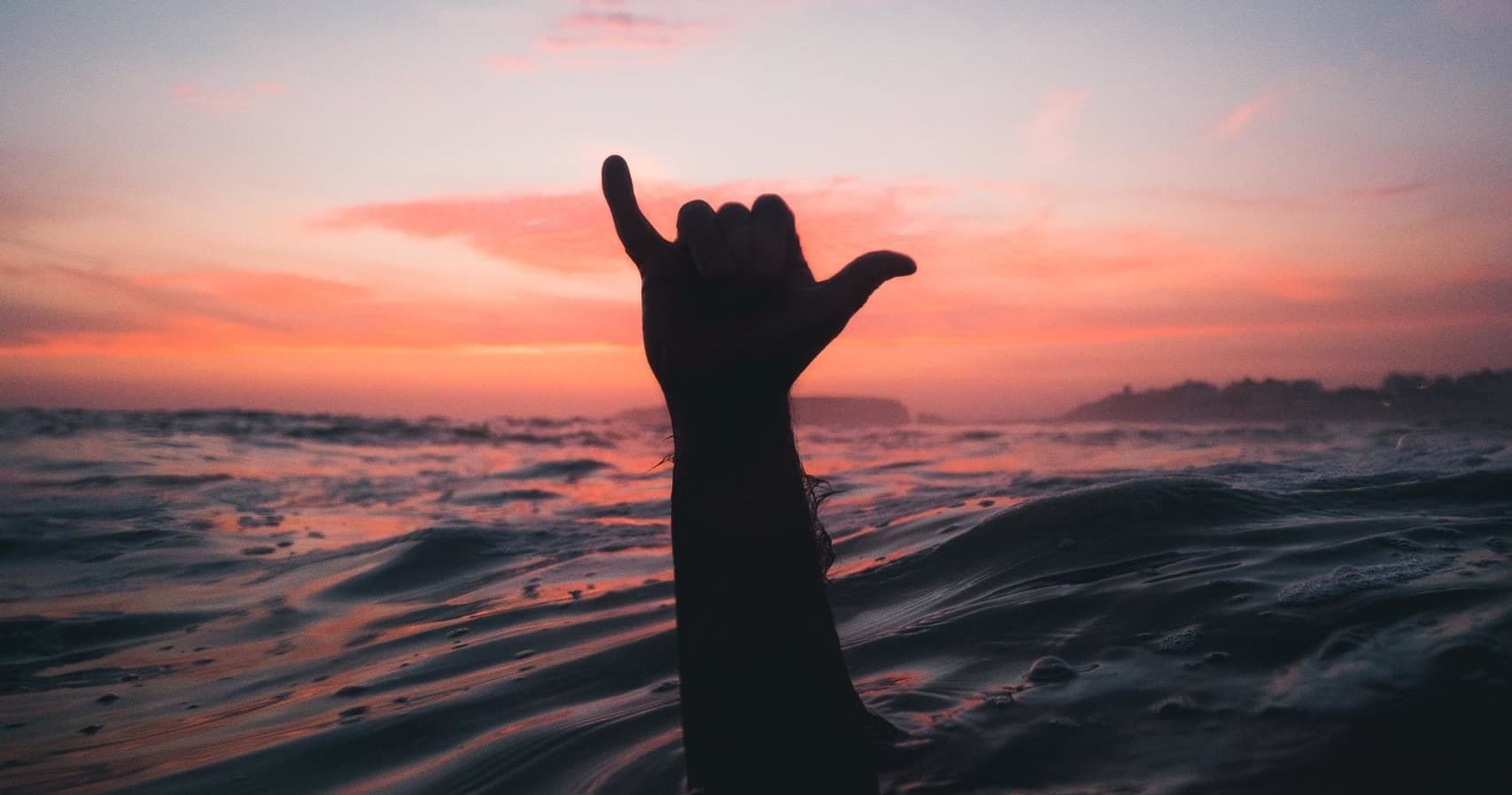 Surfer hand shaka at ocean sunset, open-water surf session