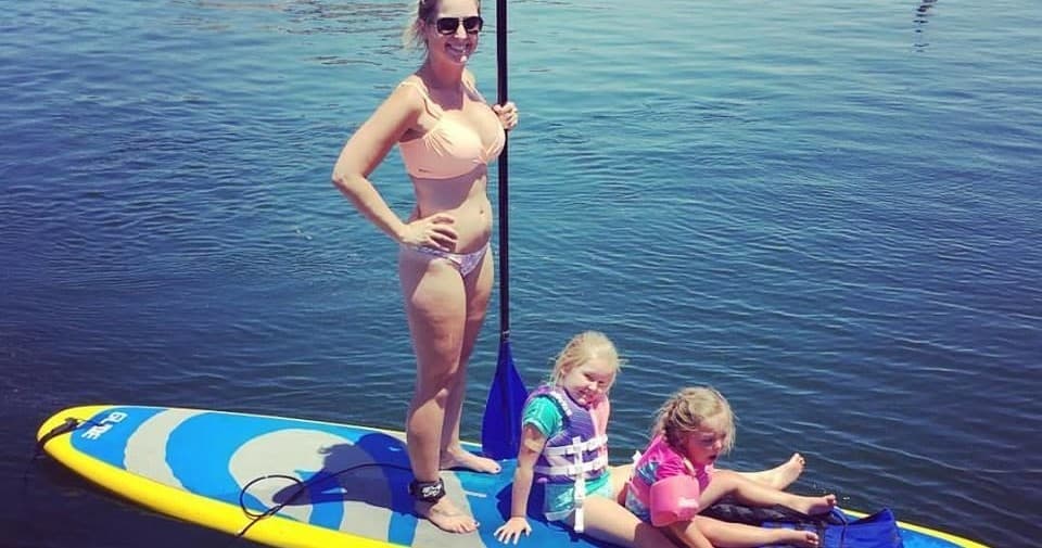 Woman and children on paddleboard relaxing on calm lake water