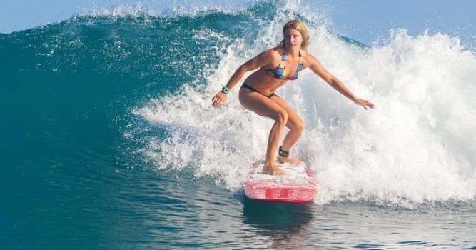 Female surfer carving a wave on bright red surfboard in ocean