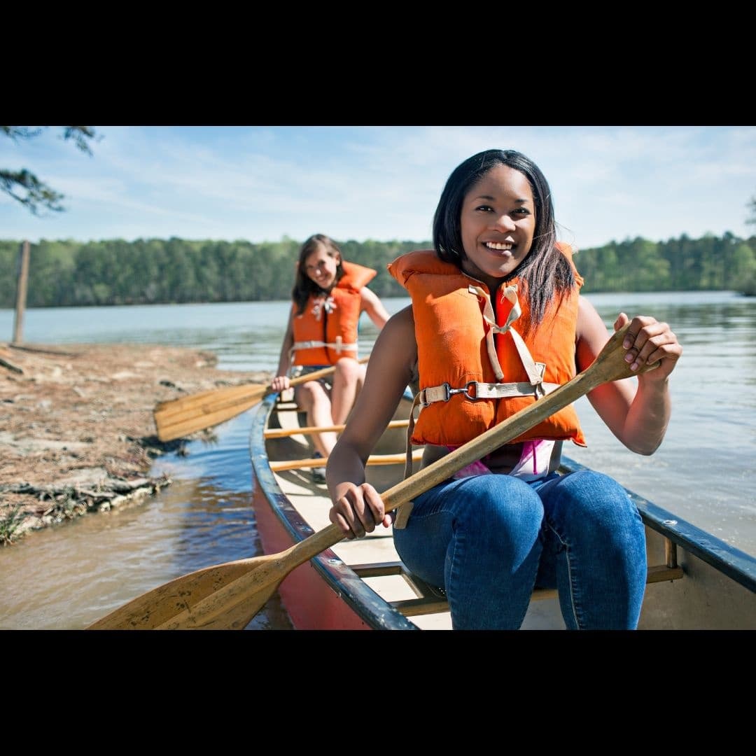 Canoeists paddling along tranquil lake shore wearing life jackets