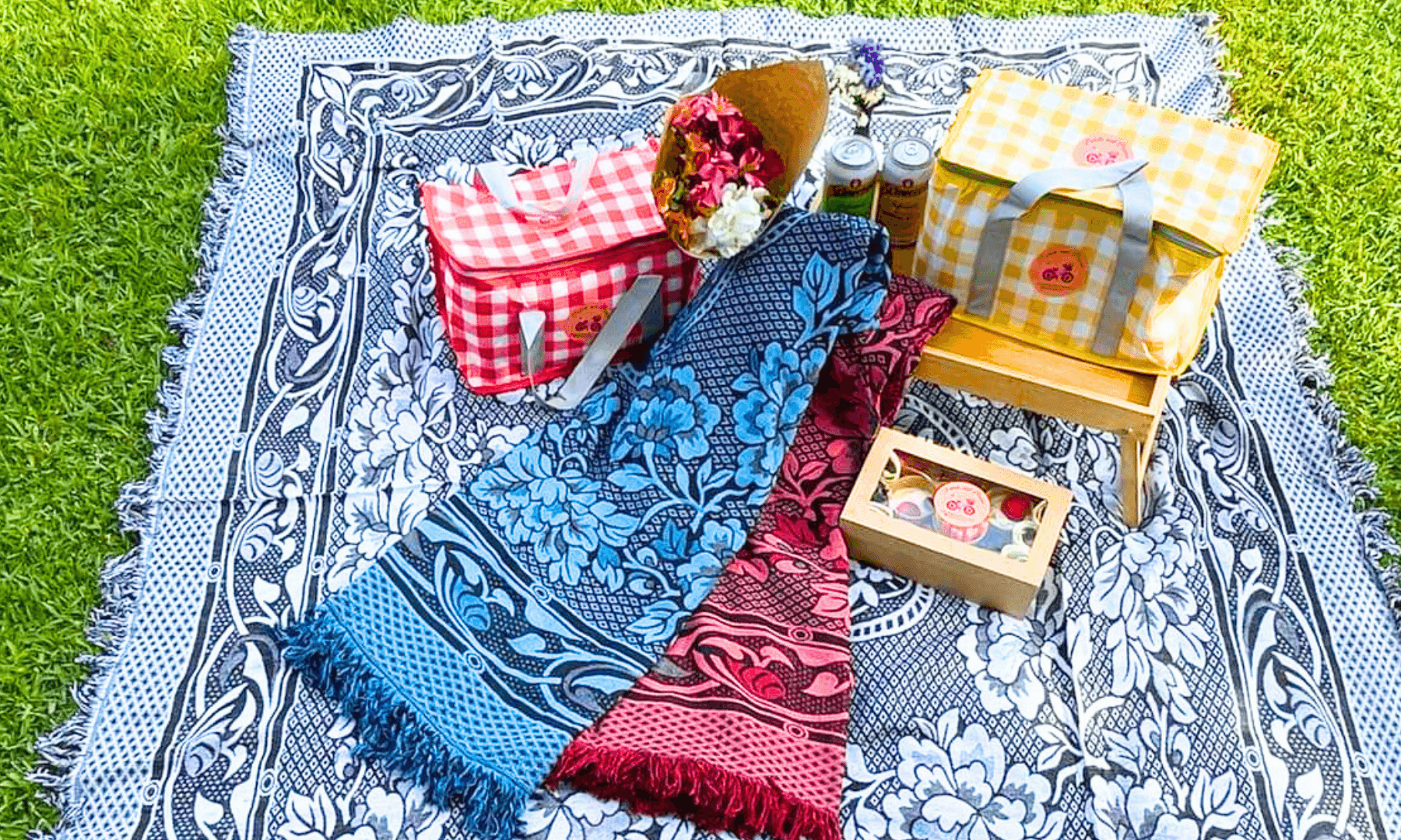 Colorful picnic blanket with baskets and scarves on park grass