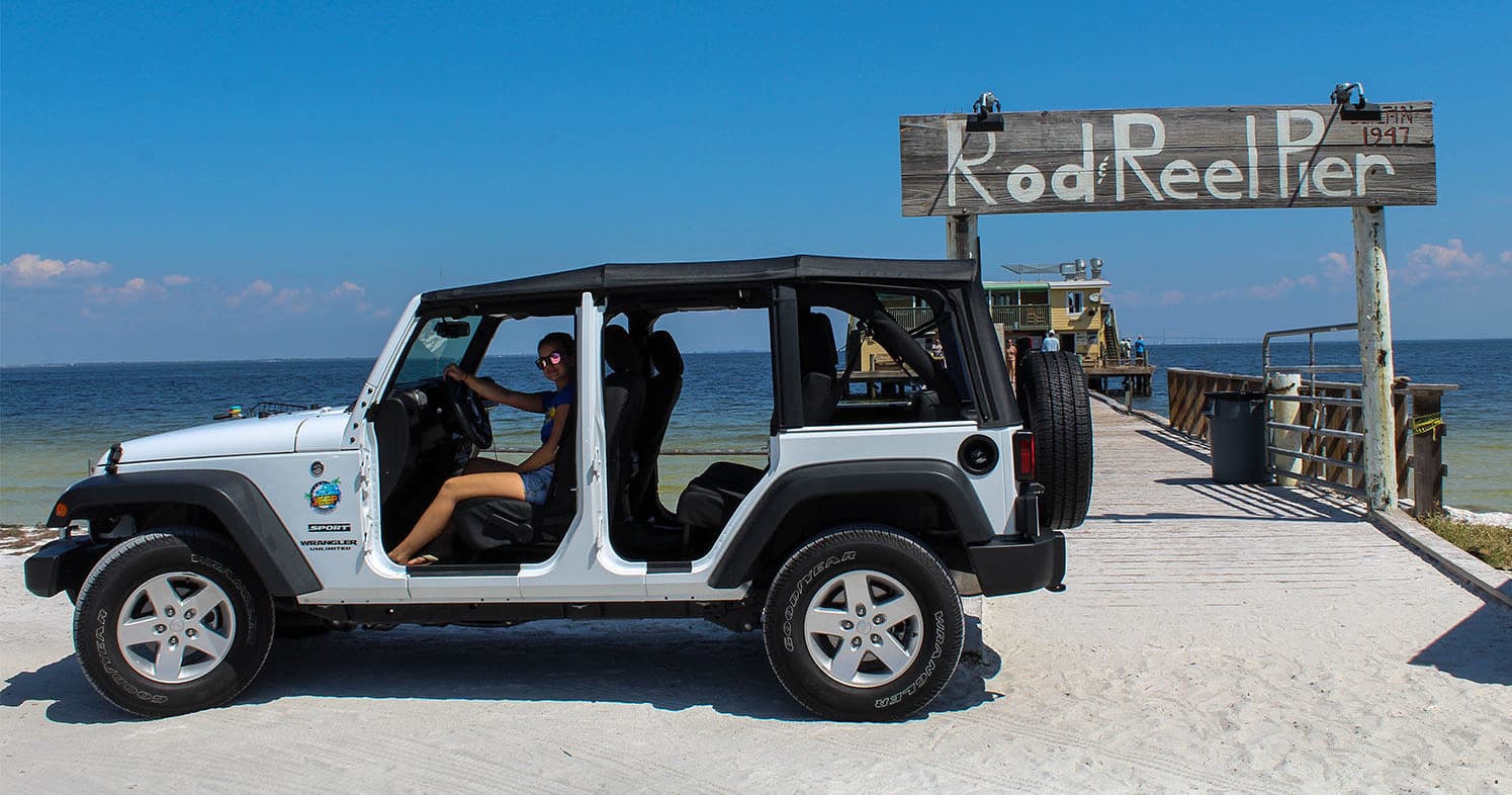 Open-door Jeep by pier on sandy beach highlighting coastal tour