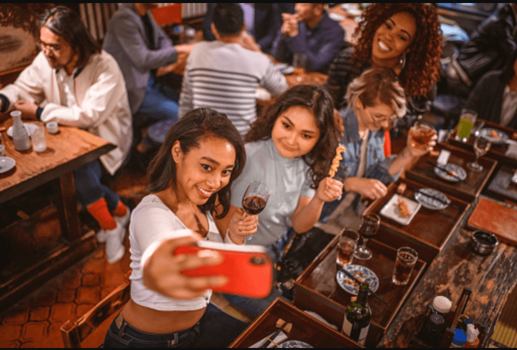 Friends taking selfie at lively indoor restaurant bar gathering