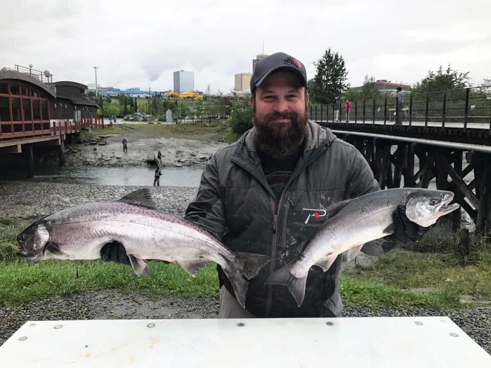Angler holding two large Chinook salmon by river and bridge