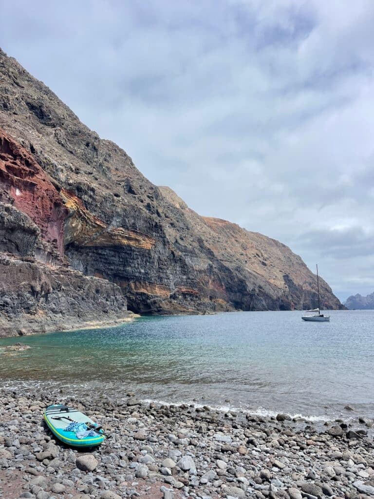 Paddleboard on rocky beach beneath towering coastal cliffs