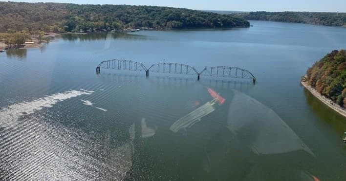 Aerial view of curved bridge and boat wake across Grand Lake shoreline