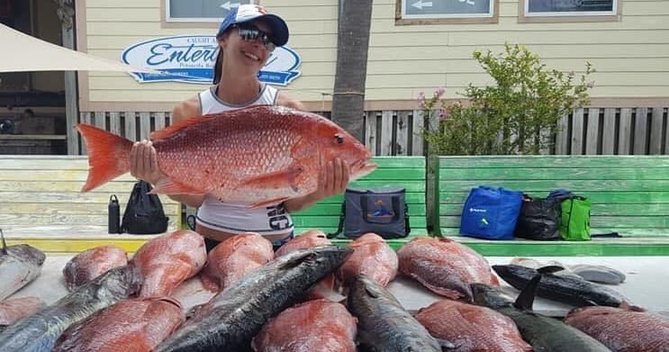 Fisher holding red snapper amid piled catch at dock
