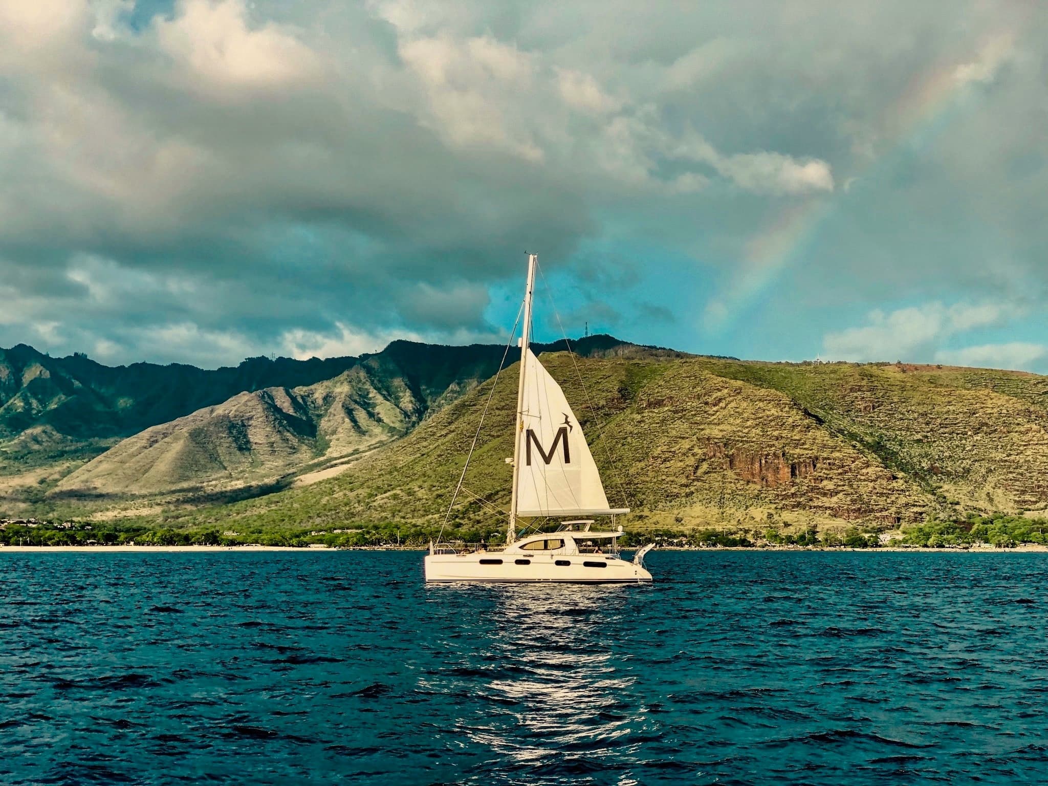 Sailboat sailing past green volcanic island and clear sea