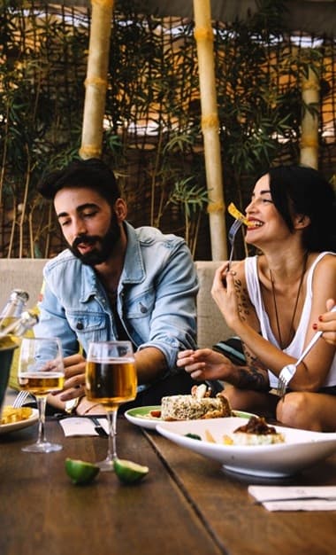 Couple enjoying outdoor patio meal and drinks at leafy cafe