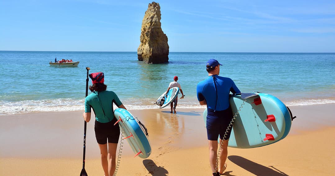 Paddleboarders carrying boards toward ocean under clear sky