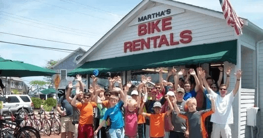 Group of riders waving outside Martha's Bike Rentals shop