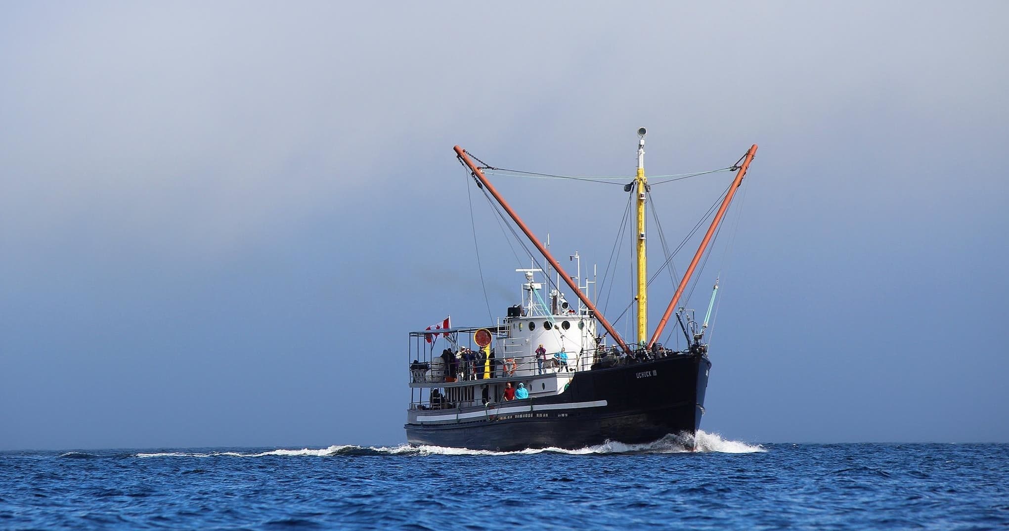 Small expedition boat sailing along open ocean near rugged coast