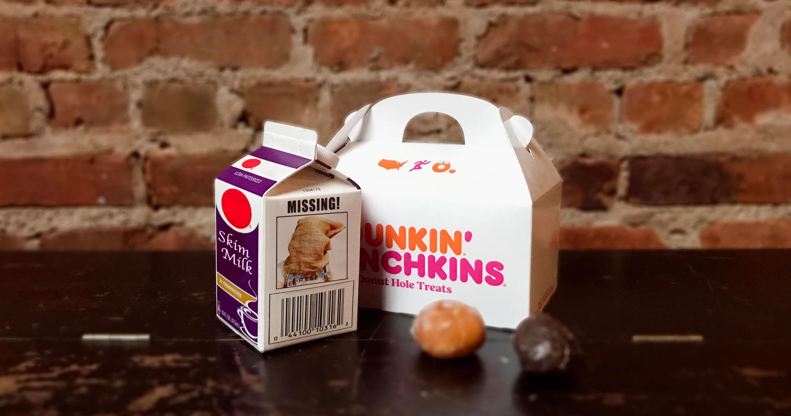 Dunkin Munchkins box and milk carton on rustic table with brick wall