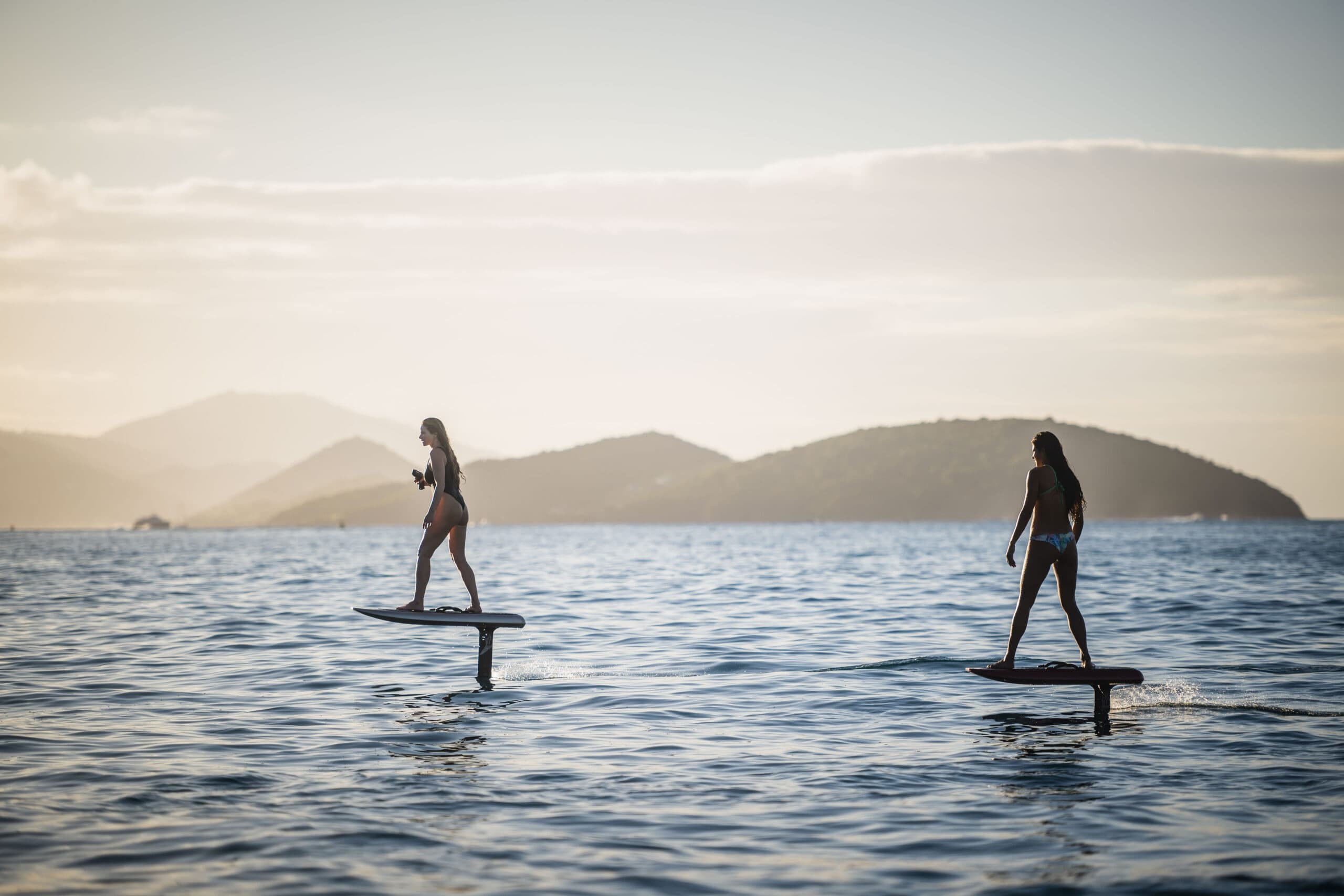 Two riders e-foiling over calm sea with distant island