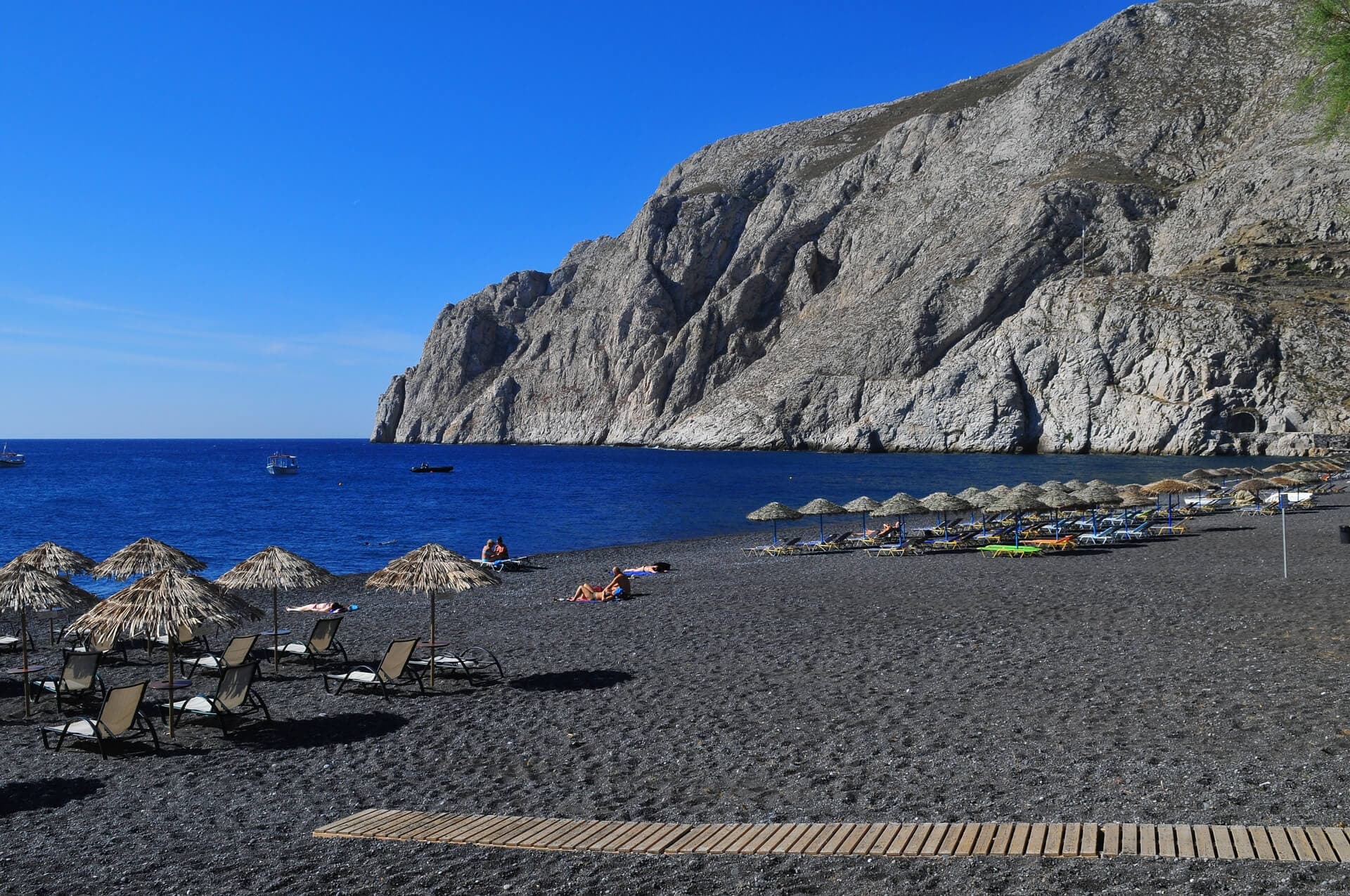 Black sand beach with umbrellas and volcanic cliffs in Santorini