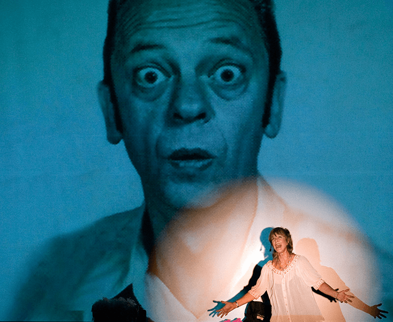 Theater performer illuminated by projected face during indoor show