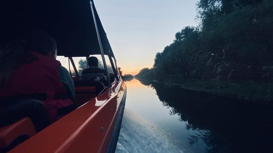 Speedboat cruising at sunset on a calm river, jungle banks