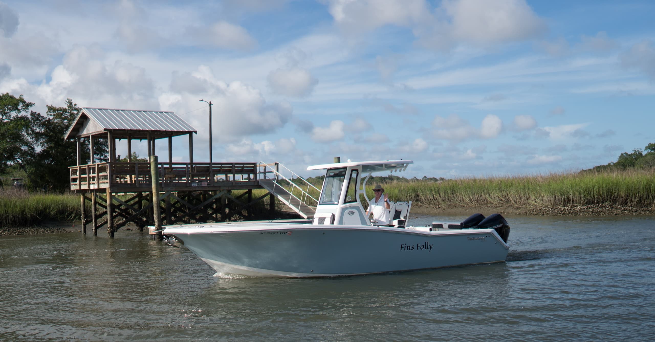Center console boat cruising by marsh dock on sunny day