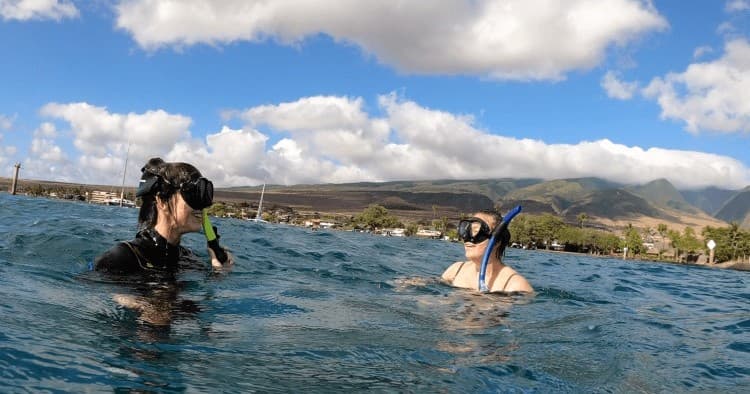 Two snorkelers floating in coastal ocean with mountain backdrop
