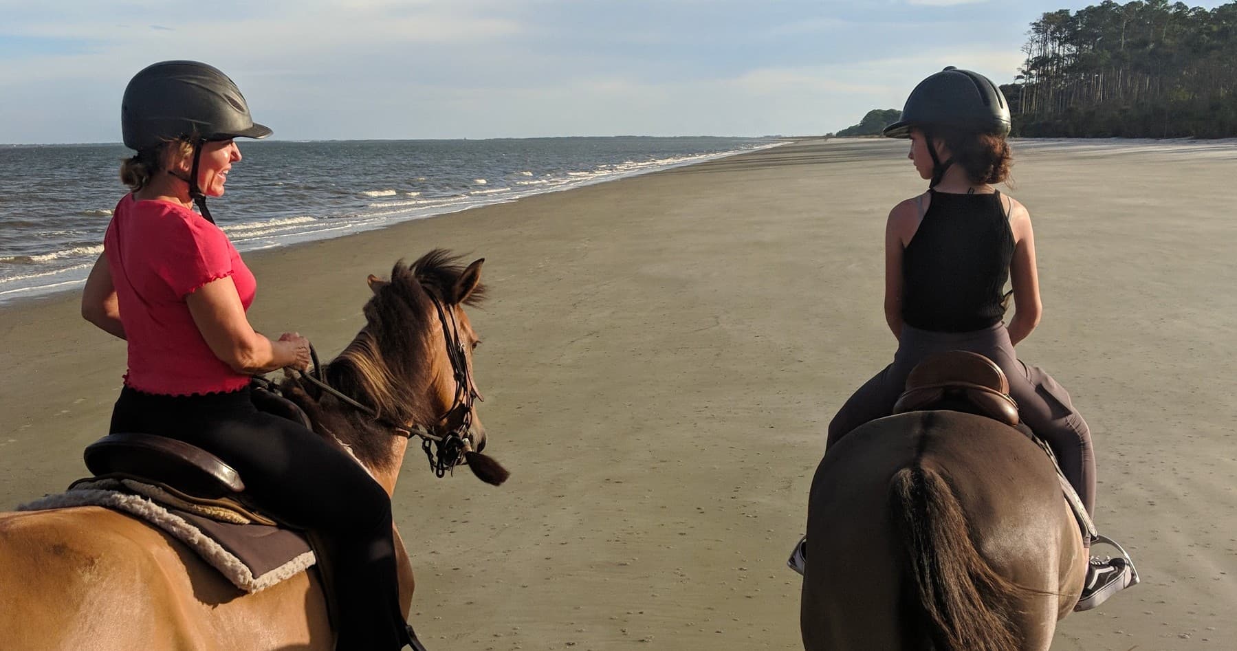 Two riders horseback beach riding along open ocean shoreline