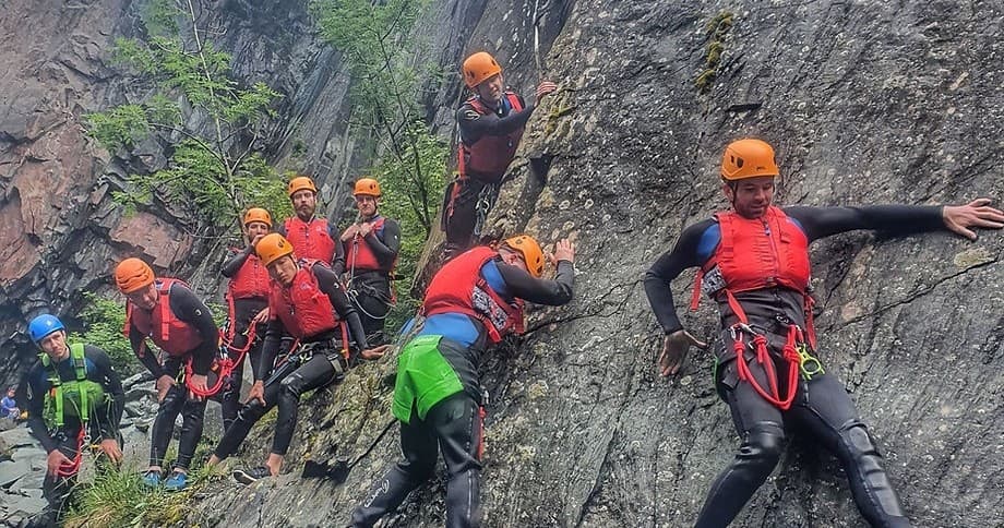 Canyoning group traversing steep rock wall in mountain gorge