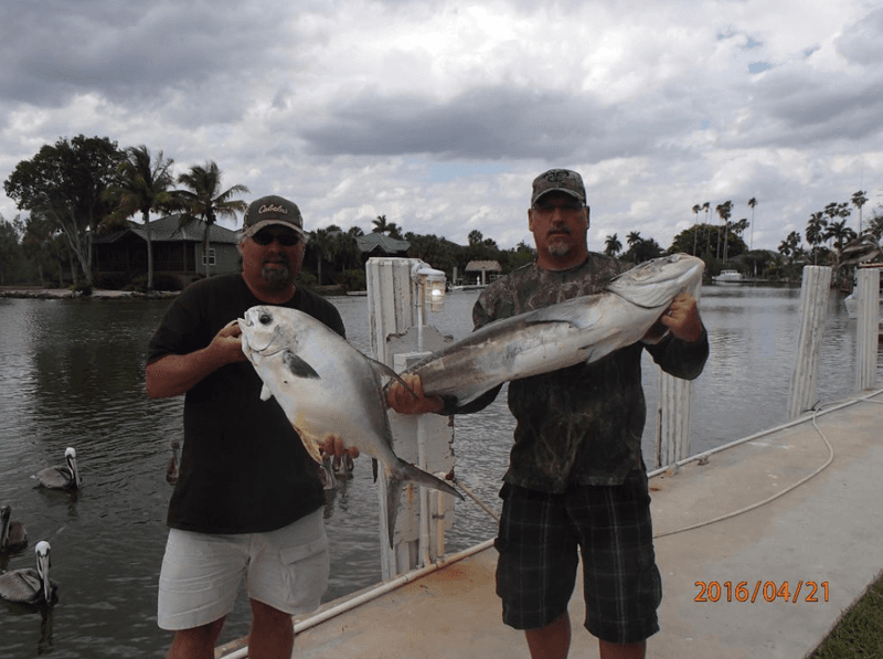 Two anglers showing catch on marina dock under cloudy sky