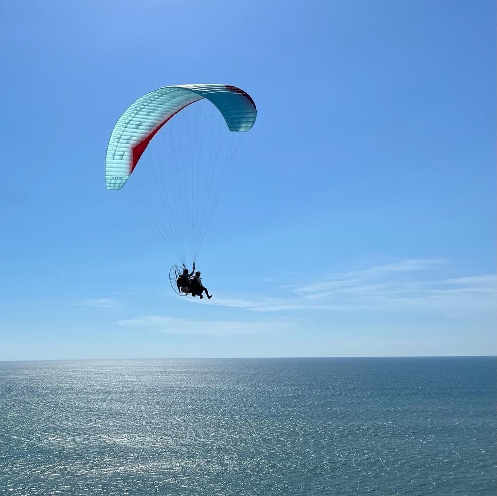 Single paraglider gliding above calm blue sea and clear sky