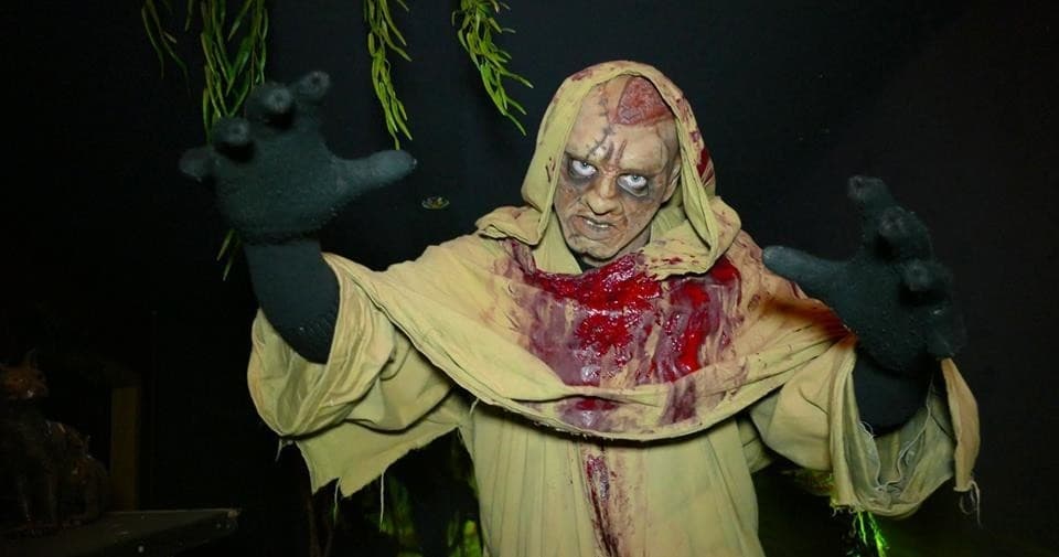 Actor in bloodied robe reaching out inside haunted house scare scene