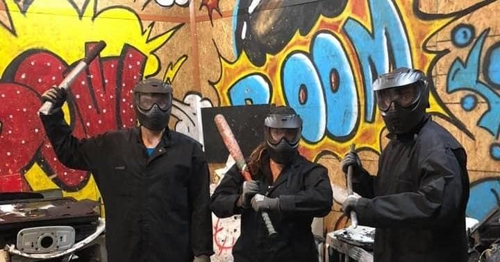 Staff in protective gear posing with bats in urban indoor smash room