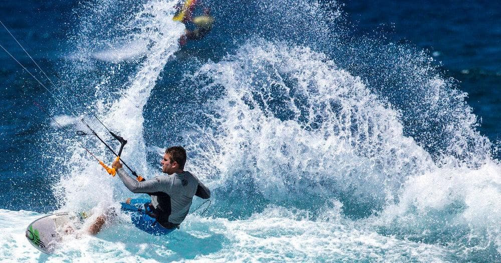 Kitesurfer throwing spray while maneuvering near ocean swells