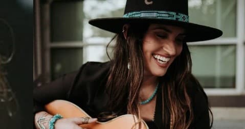Woman playing acoustic guitar outdoors on porch, smiling warmly