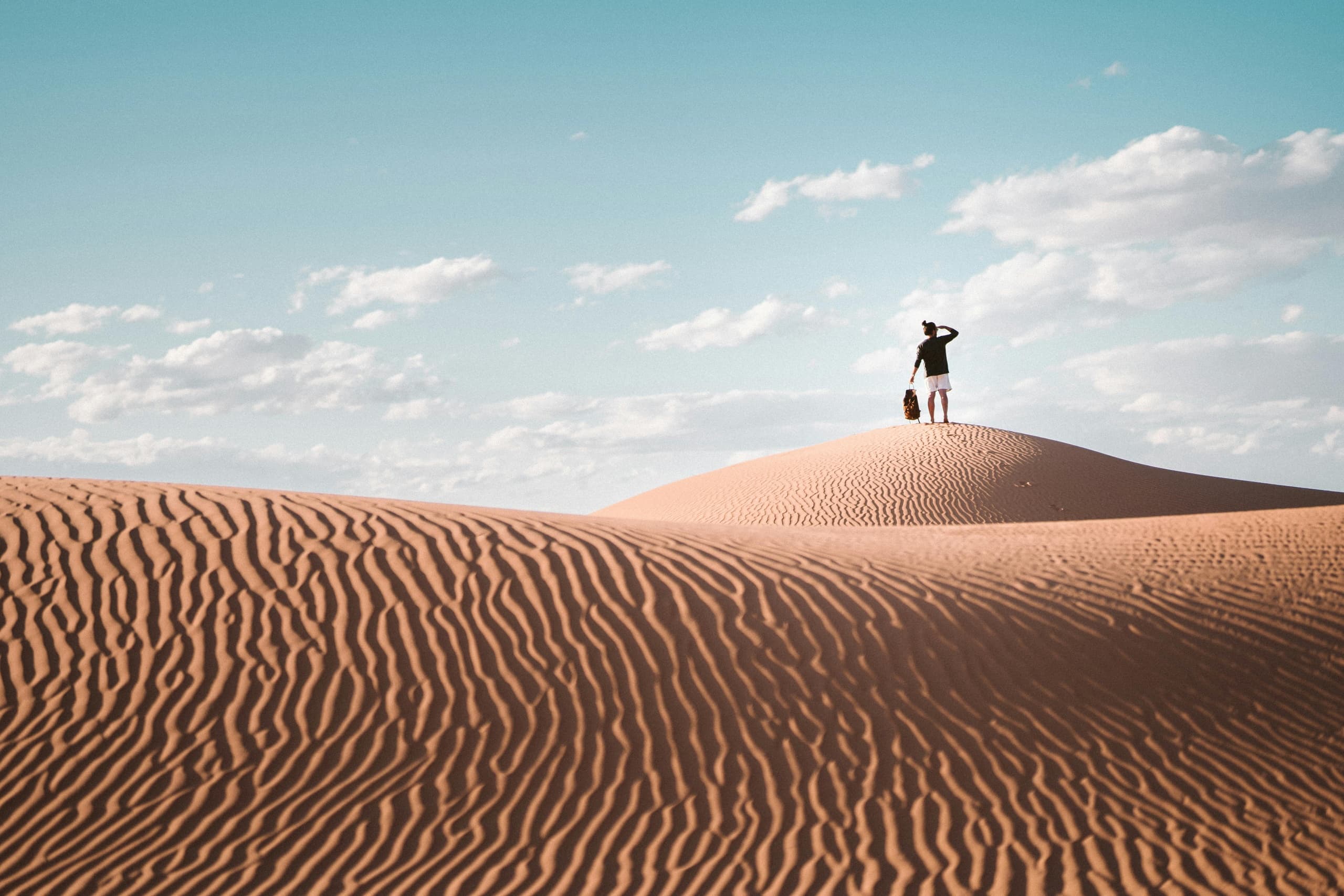 Lone traveler atop expansive sand dune, desert exploration