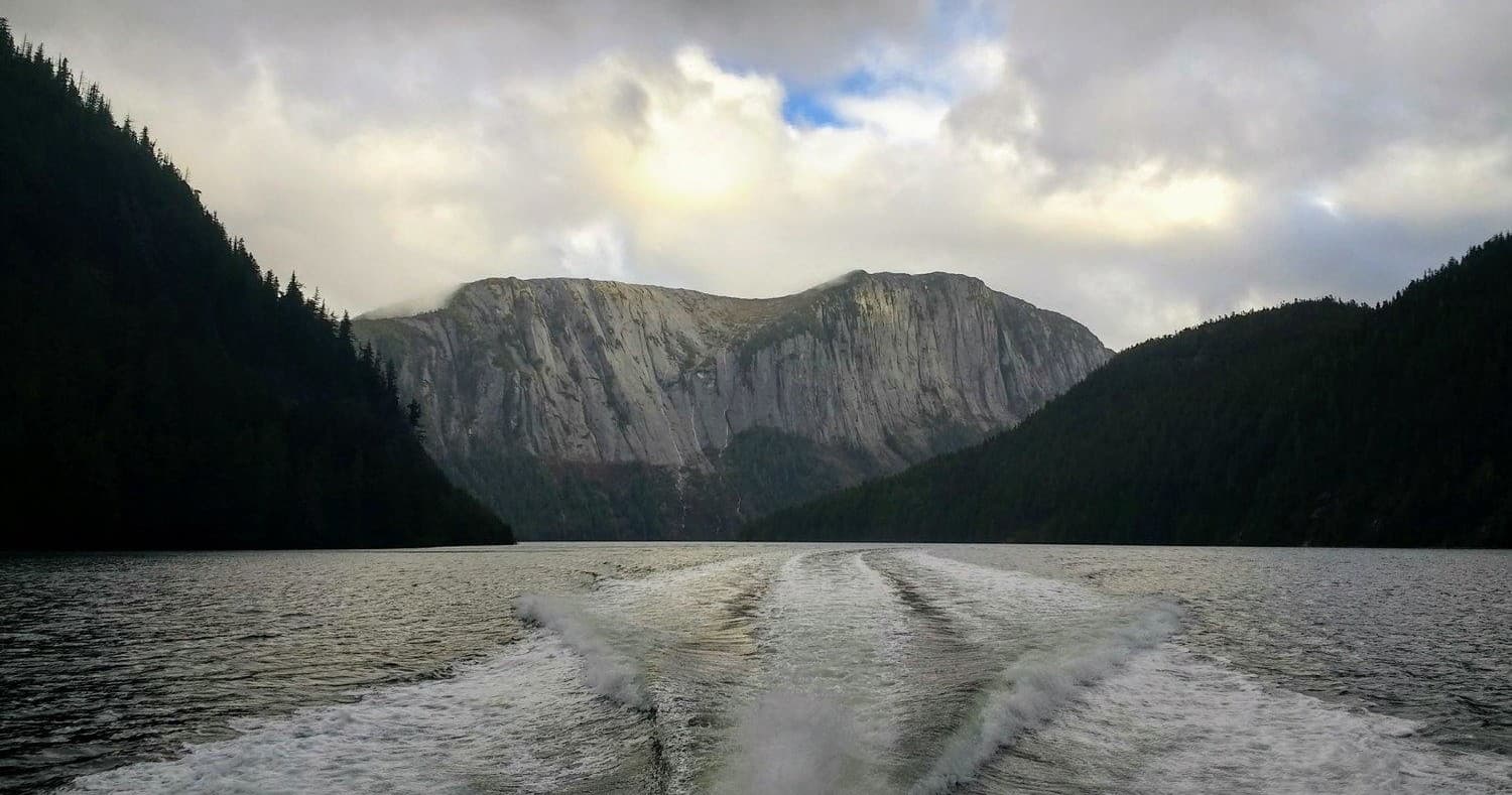 Boat wake in Alaskan fjord with dramatic granite cliffs
