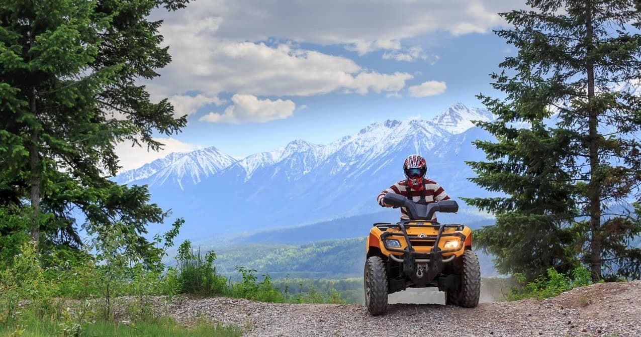 ATV rider on mountain trail with snow-capped peaks view