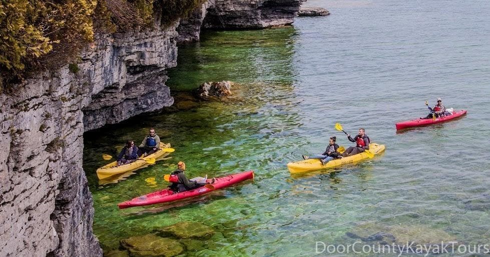 Guided kayaks paddling along scenic cliff alcoves on lake