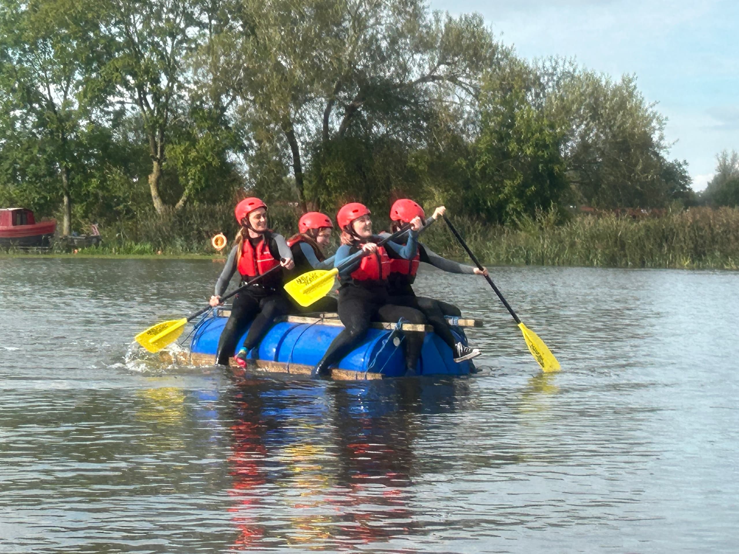 Group rafting on a calm lake wearing helmets and paddling