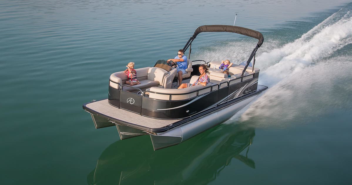 Pontoon boat speeding across green lake with happy riders
