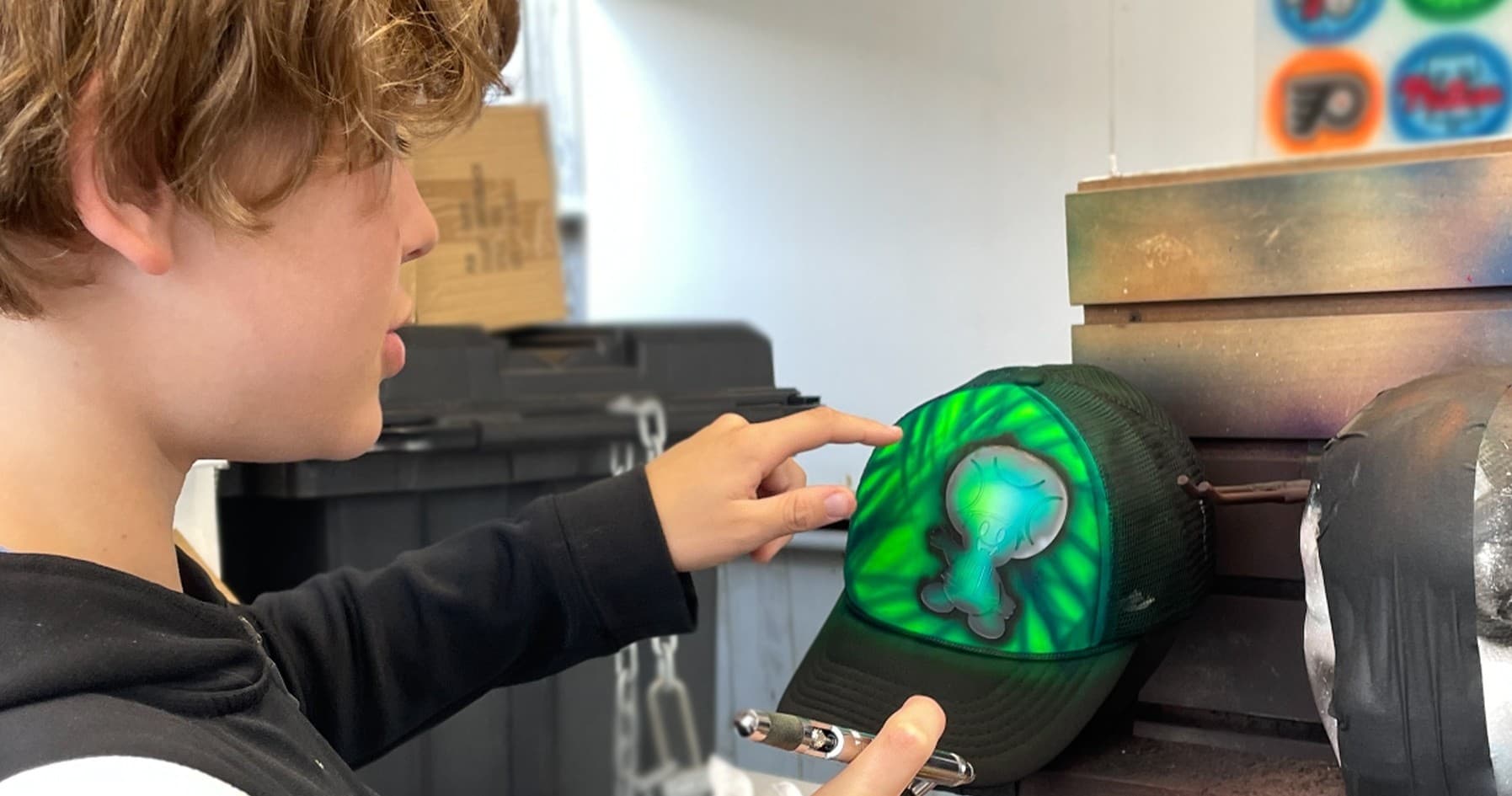 Teen airbrushing green surf logo on trucker hat in studio
