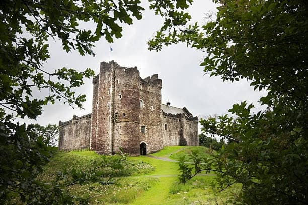 Ancient castle ruins framed by trees on verdant Scottish countryside walk