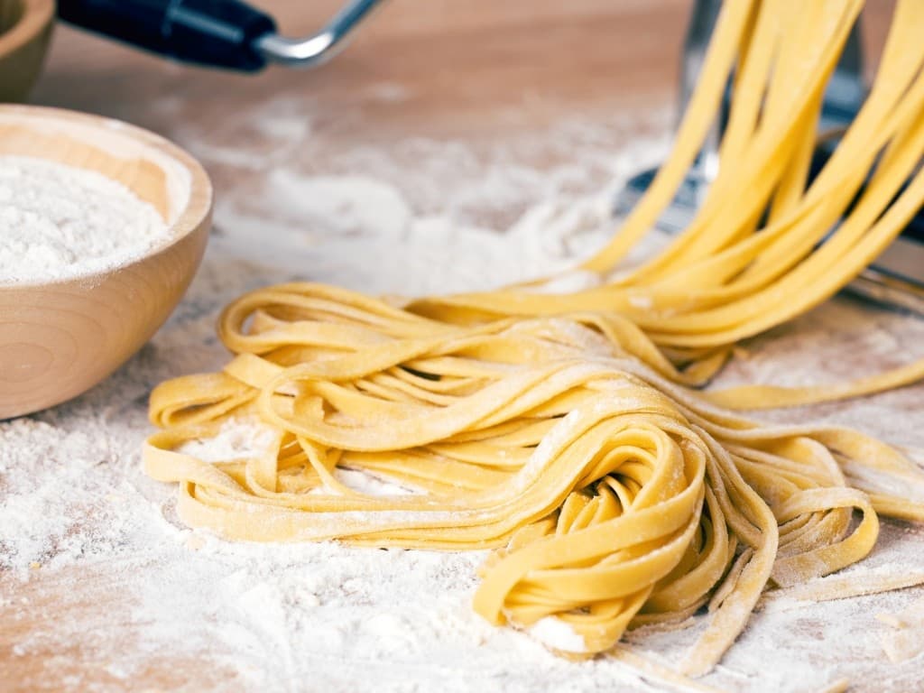 Fresh hand-cut tagliatelle pasta on floured board, rustic prep