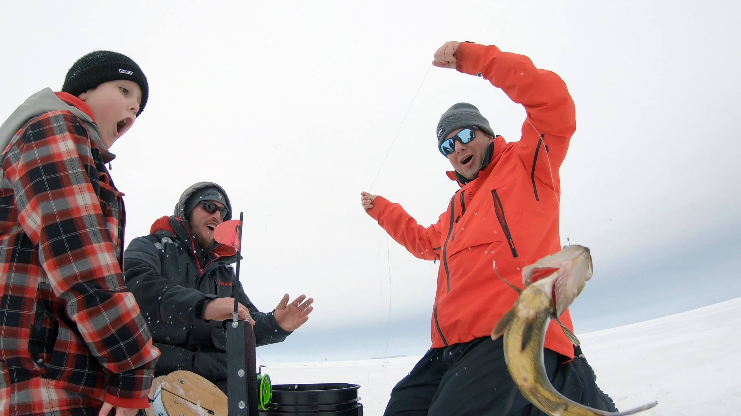 Ice fishing group pulling fish through hole on frozen lake