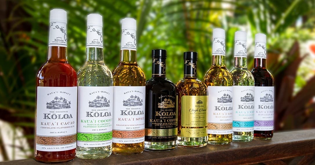 Koloa rum bottles displayed outdoors on wooden railing in tropical garden