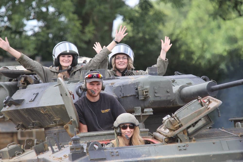 Visitors waving from open tank hatch during countryside tour