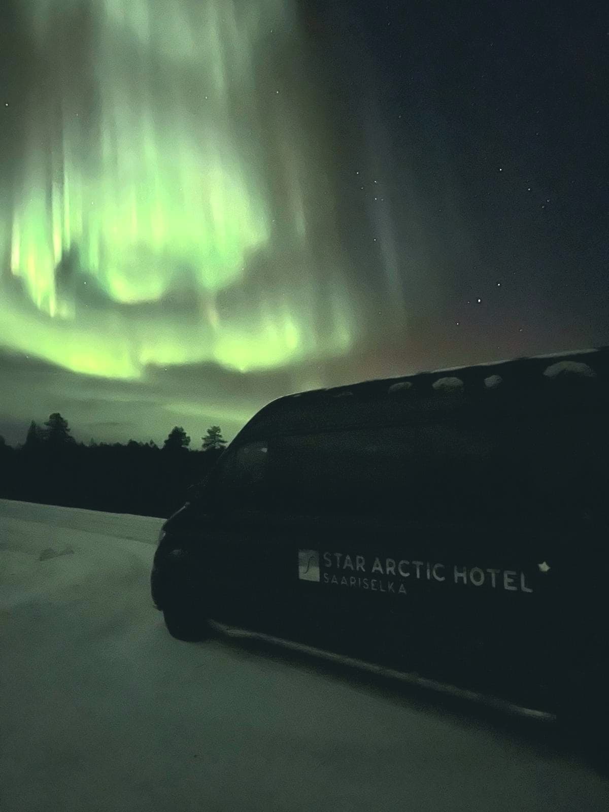 Green aurora glowing above Arctic van on remote winter road