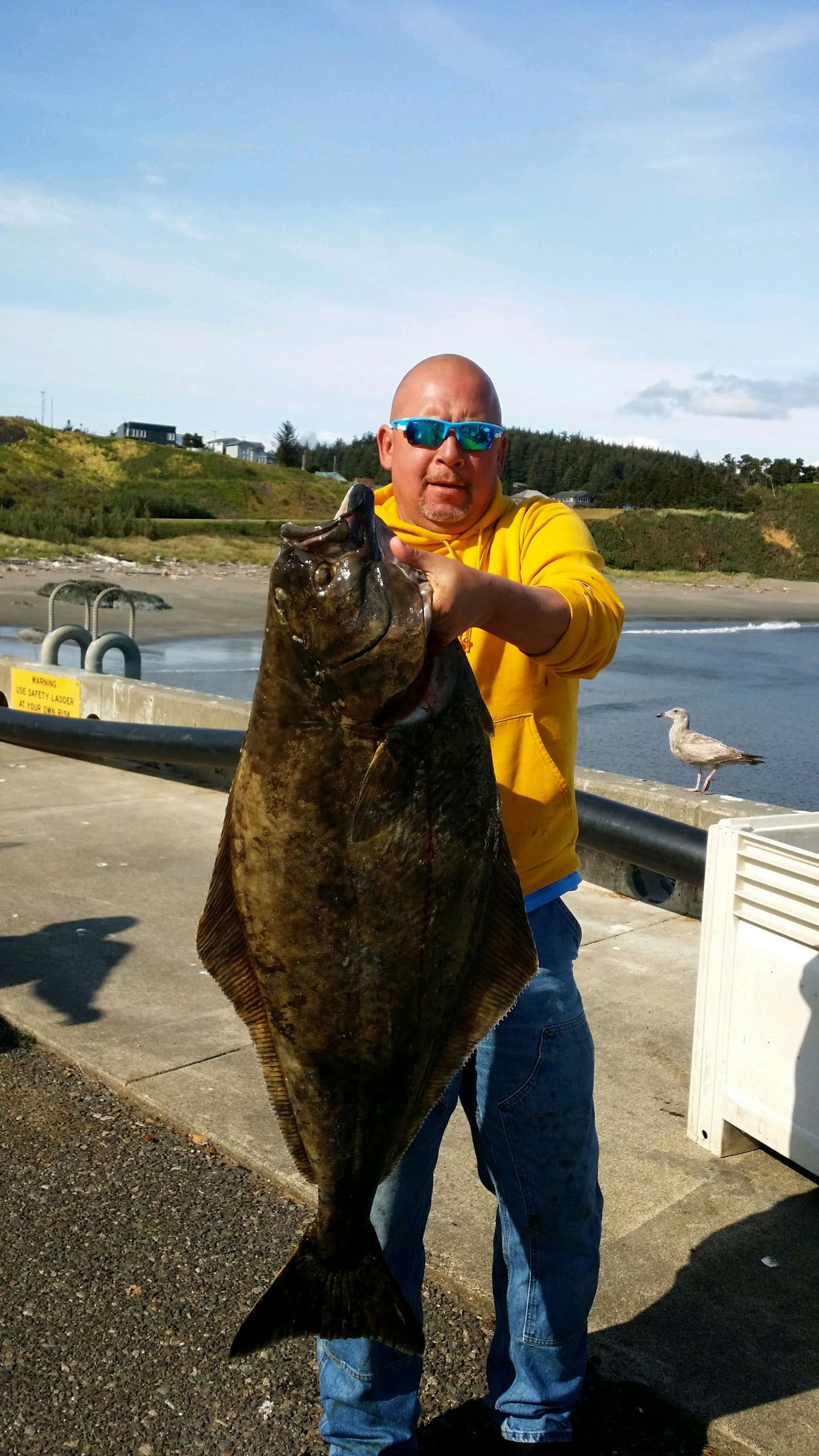 Angler holding giant halibut on coastal dock after charter trip