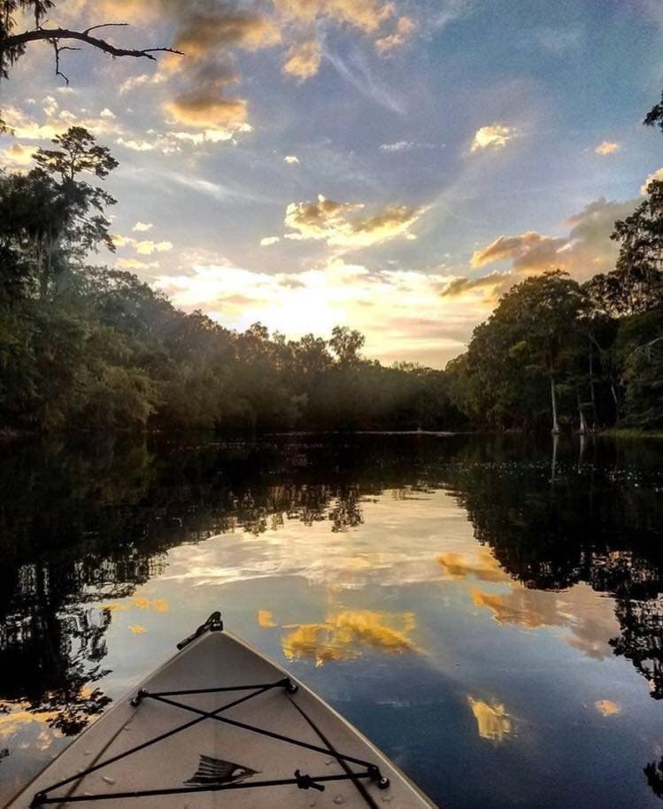 Kayak bow reflecting sunrise on glassy river through forest