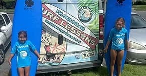 Two children posing with surfboards by company lesson van