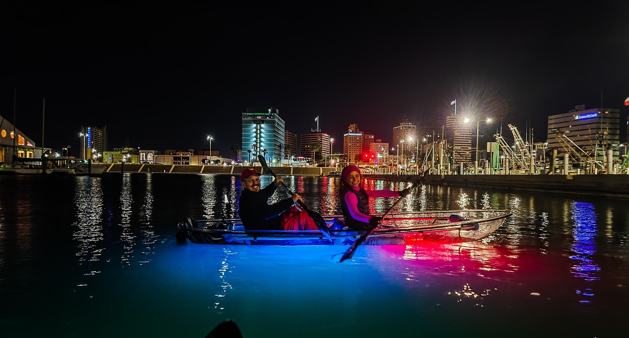 Nighttime city marina kayaking with vibrant LED-lit boats