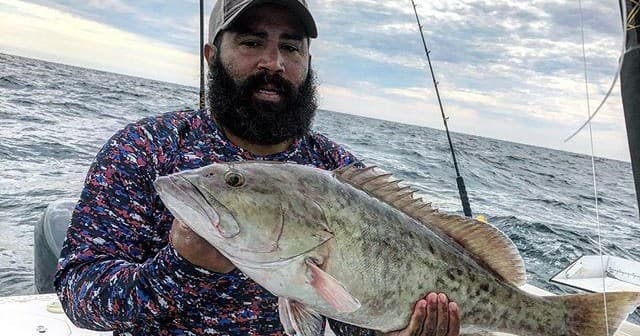 Angler holding large grouper on offshore charter boat at sea