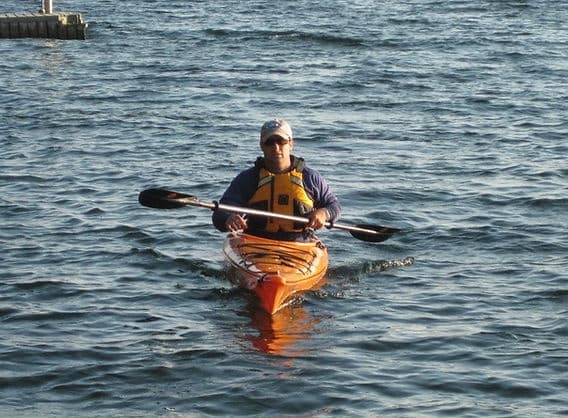Kayaker paddling single orange kayak on open lake water